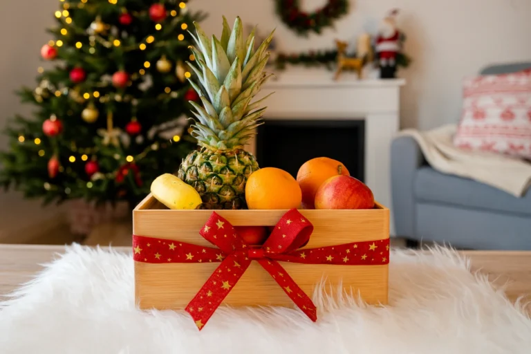 Bambusa dāvanu kaste ar augļiem, apsieta ar sarkanu Ziemassvētku lenti, svētku noformētā dzīvojamā istabā ar eglīti fonā.